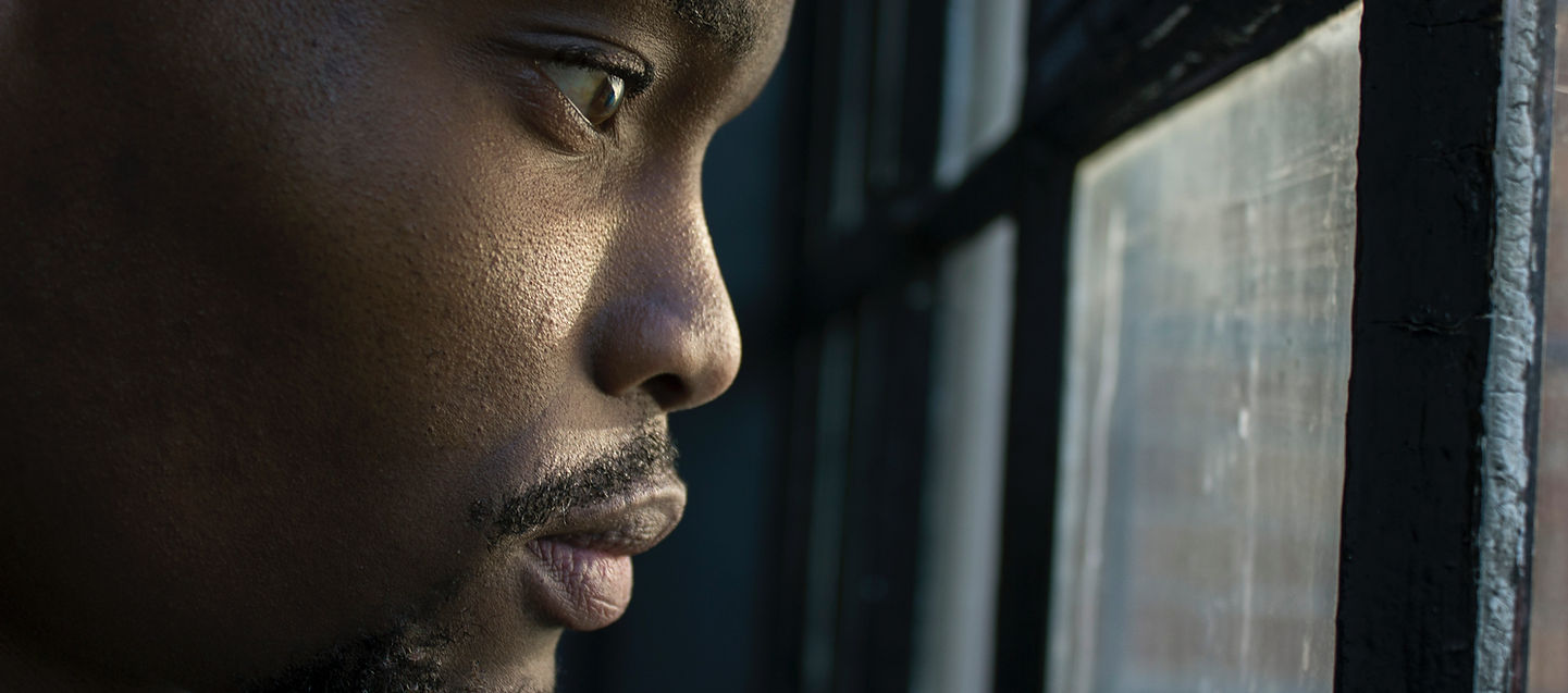 Focused man staring out window, symbol of reflection before execution.