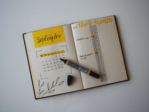 Open planner with "September" calendar and "this month" tasks on a table. Yellow accents, a marker, and a cap nearby.