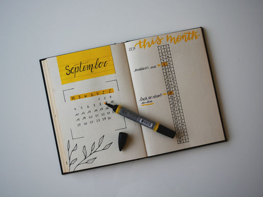 Open planner with "September" calendar and "this month" tasks on a table. Yellow accents, a marker, and a cap nearby.