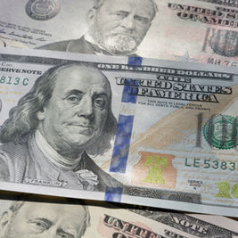 Close-up of overlapping U.S. $100 bills with Benjamin Franklin, blue security strip, and visible text United States of America and 100