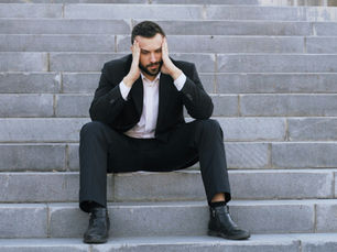 Man sat on concrete steps holding his head, visibly stressed