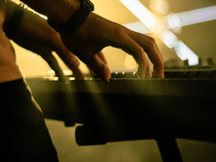 Hands playing a keyboard in dim lighting, with a golden glow and light beams in the background, creating an atmospheric mood.