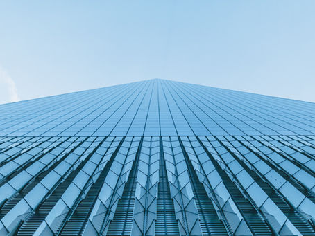 Looking up at a tall, glass skyscraper against a clear blue sky. The building's reflective panels create a geometric pattern.