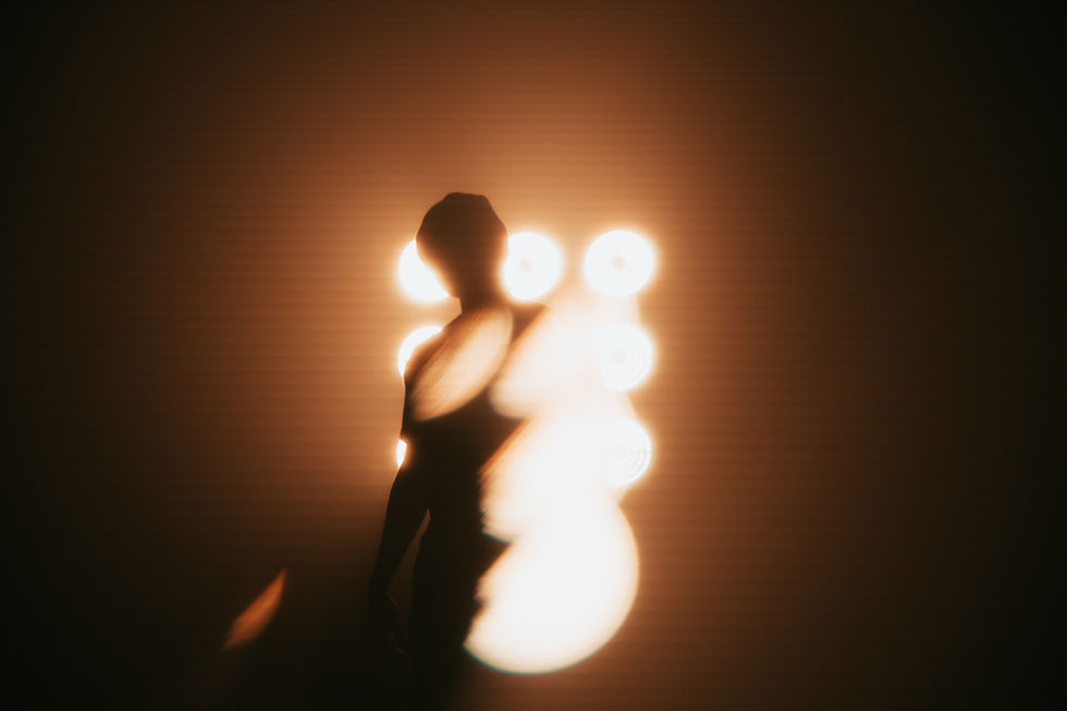 Silhouette of a person against bright circular lights in a dark, blurred setting, creating an abstract and mysterious mood. Minimal details.