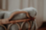 Close-up of a wicker chair draped with a chunky gray knit blanket, with soft beige background and a cozy, calm mood