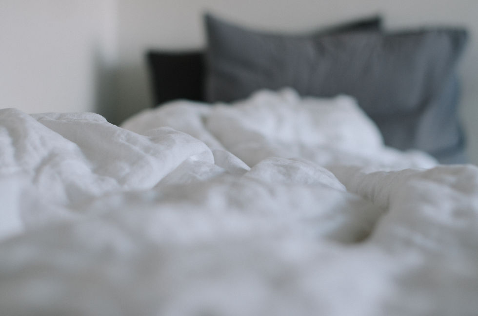 Close-up of white, crumpled bedding with gray pillows in the background, creating a soft and cozy atmosphere.