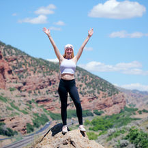 A person standing confidently outdoors with arms raised, representing strength, movement and body confidence.