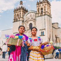 Hispanic women in traditional Mexican attire with cathedral in background.