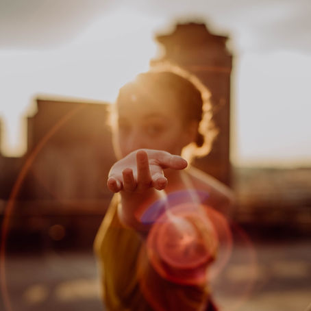 dancer reaching  their hand gently towards the camera with the sunset glaring in the background with buidlings