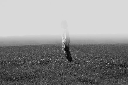 Person standing in a foggy field, partially obscured by mist. Monochrome tones create a mysterious and serene mood.