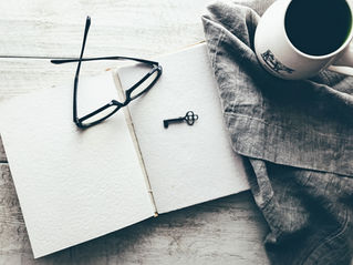 A journal opened to a blank page next to glasses, a key, and a mug