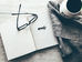A journal opened to a blank page next to glasses, a key, and a mug