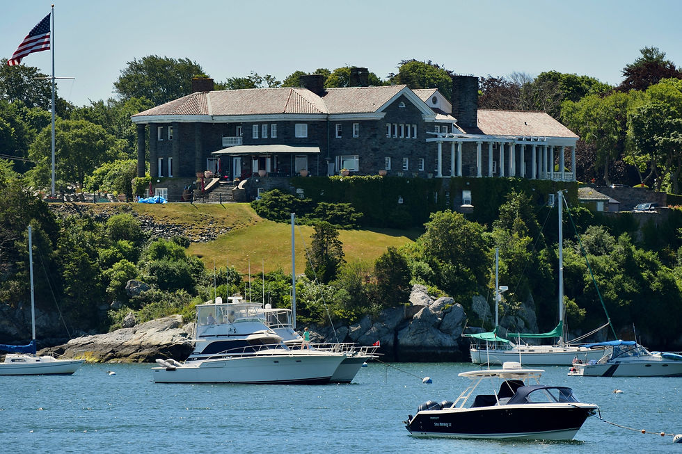 Lodge dans l'état du Maine, USA en pierre au bord de l'eau, drapeau américain déployé. Bateaux amarrés au premier plan, ciel bleu et verdure environnante.