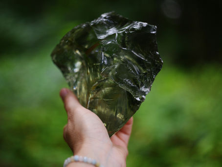 a piece of rough black obsidian crystal reflecting the green around it