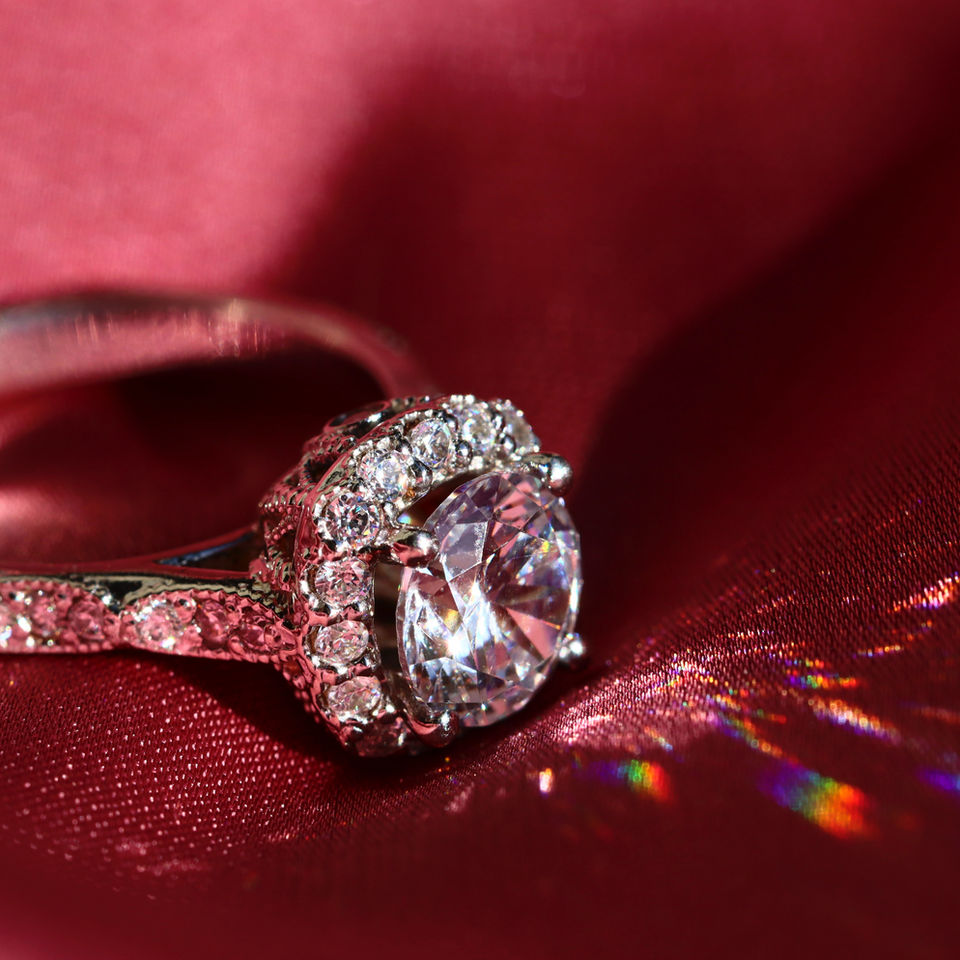 A diamond ring featuring a large solitaire diamond surrounded by smaller round brilliant cut diamonds, in white gold.