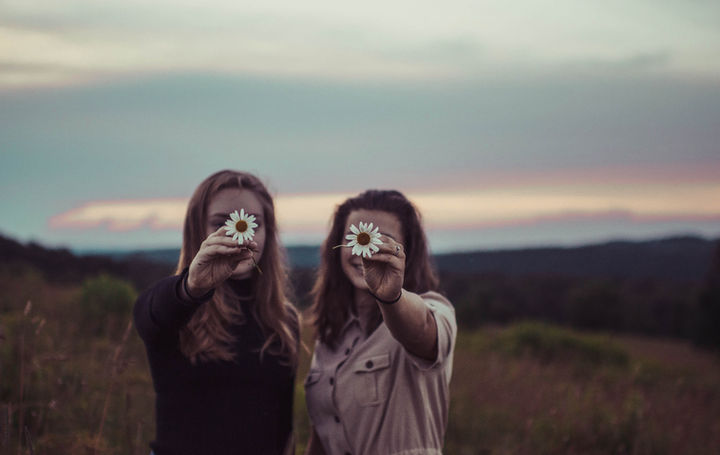 Two women in a field holding daisies