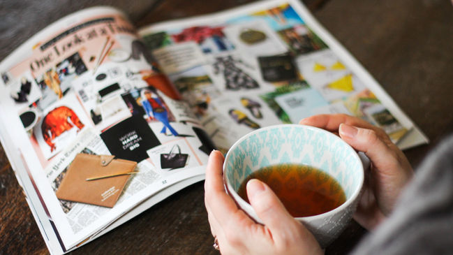A person holding a cup of tea reading a wellness magazine, representing a quick start to Ayurveda