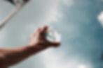 Hand holding a clear sphere against a cloudy sky, reflecting an upside-down view of an American flag. Bright, serene mood.
