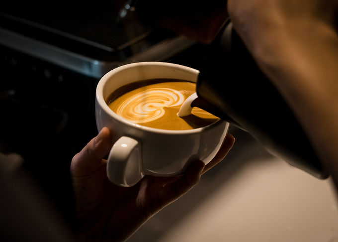 A barista pouring milk it a coffee in the shape of a heart.