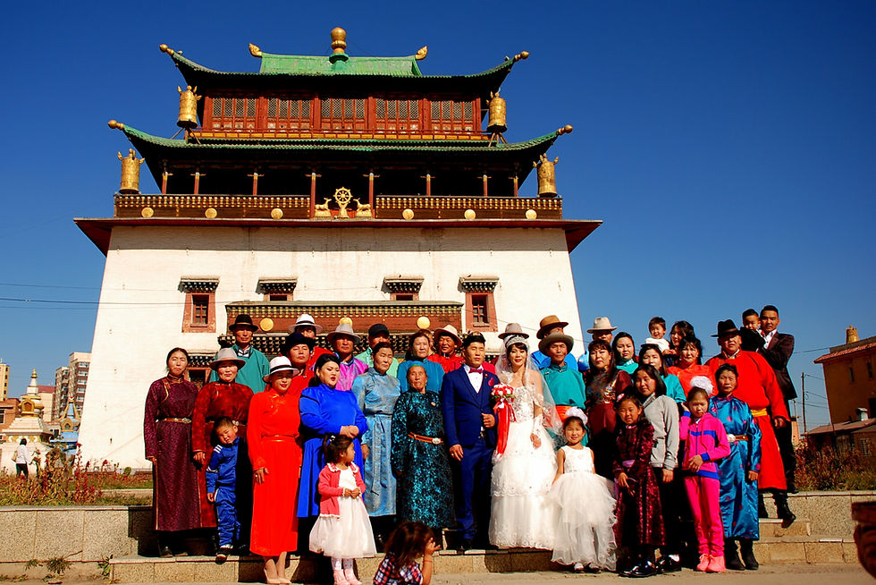 Group of people in colorful attire, including a bride and groom, pose happily in front of a traditional temple under a clear blue sky.