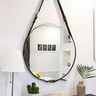 large round mirror hanging by a leather strap