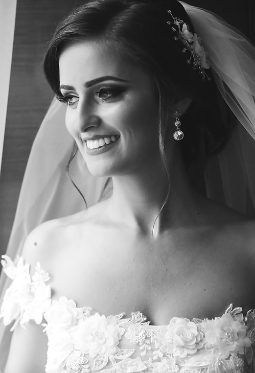 Black and white photo of a brunette bride in her wedding gown standing by the window