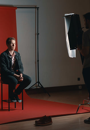 A person sitting on a set, in front of a camera.