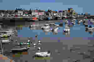 the harbour of Barfleur in Normandy, France with small boats, quayside houses and Saint-Nicolas church and a Normandy blue sky