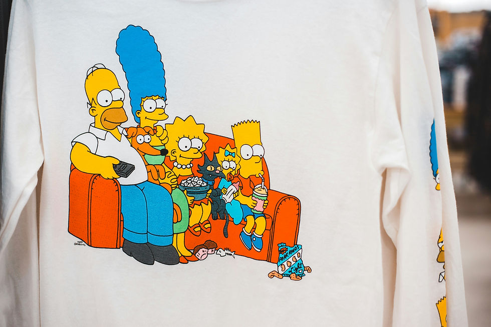 Cartoon family sitting on an orange couch eating snacks. Characters have yellow skin, blue, green, and orange clothes on a white shirt.