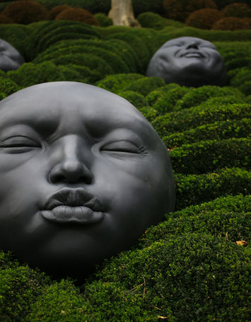 Statues of faces nested in bushes.