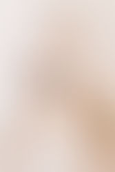 Bald mannequin with bold makeup gazes forward, set against a soft, blurred background with a second mannequin partially visible behind.