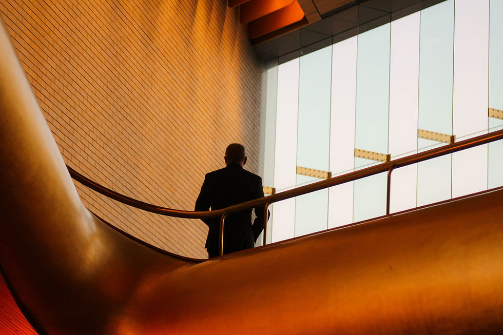 a man in a suit standing on a first floor stairwell looking out of a large glass window