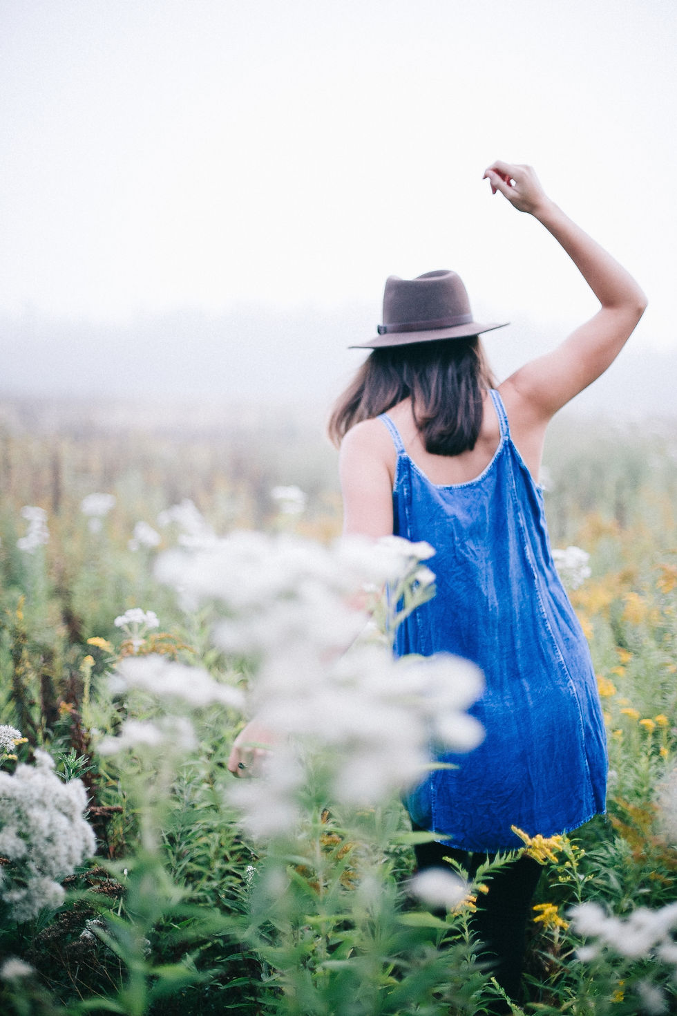 woman in blue dress and fedora walking through a field