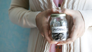 Person holding a glass jar filled with coins labeled “savings,” representing maximizing your 401(k) and building long-term retirement savings through consistent contributions and financial planning.
