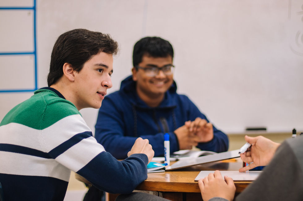 Boys sitting at a table with school work look a someone off camera and smile.