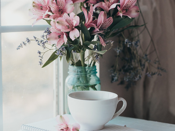 cup of tea sitting on a notebook with flower bouquet