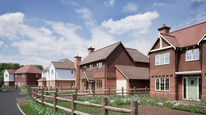 Row of new brick and white houses along a quiet street with wooden fences, wildflowers, and a bright cloudy sky.