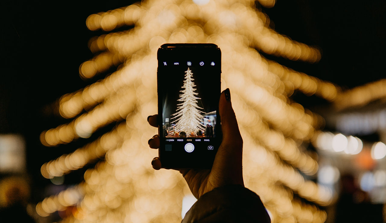 Someone taking a picture of a lit christmas tree on their phone at a UK seasonal event
