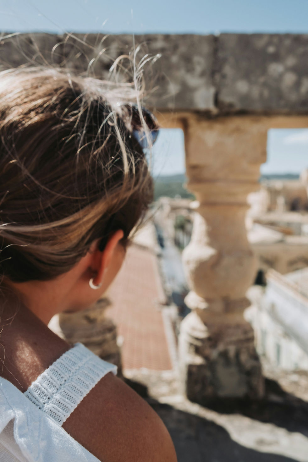 Woman peeking through columns to look at a view over rooftops.