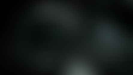 Close-up of a camera lens labeled "Carl Zeiss Jena Tessar 2.8/50" on a laptop keyboard. Dark, moody lighting with soft reflections.