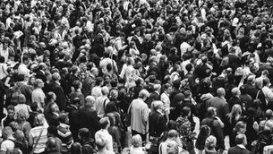 Black-and-white crowd of commuters and pedestrians packed shoulder to shoulder in a busy public square