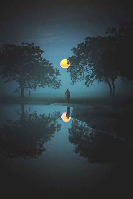 A lone figure under a streetlight reflected in water, capturing the mysterious and deep emotional work of exploring the hidden self.