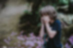 A child in a field covering his eyes with his hands