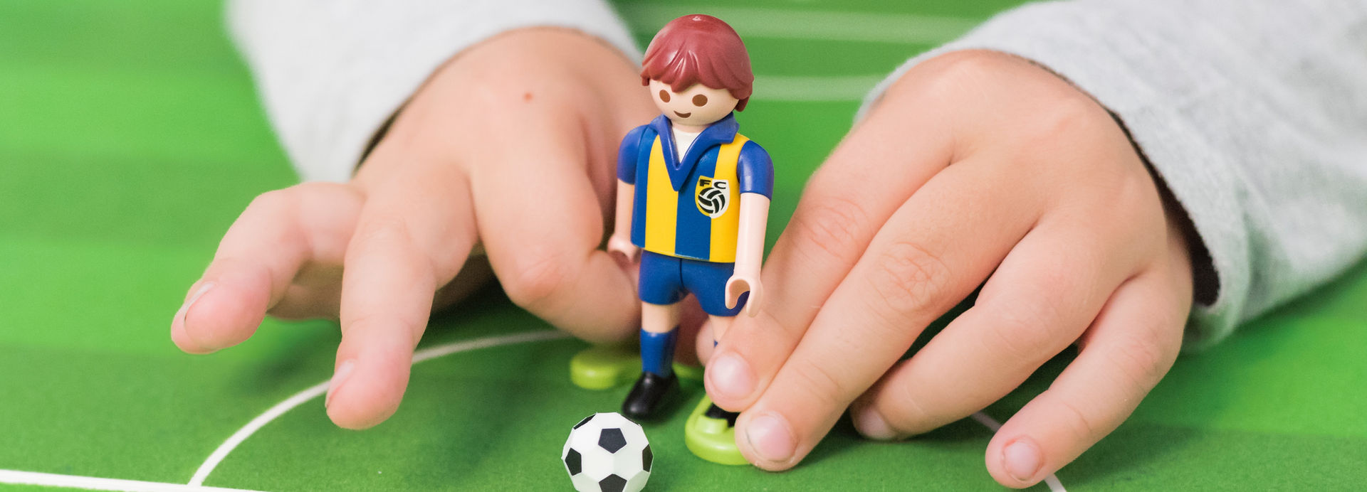 A child's hands playing with a toy soccer player.