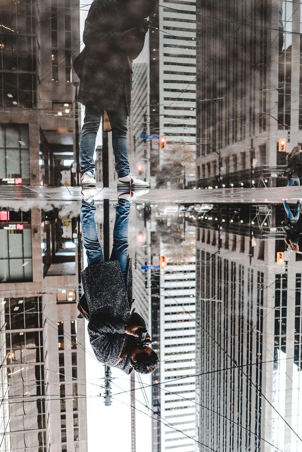 Sokak fotoğrafçısı, yerdeki su birikintisini kullanarak yansıma fotoğrafı çekiyor.