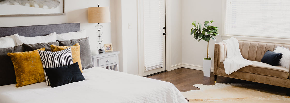 A stylish bedroom retreat featuring plush textiles, a grey headboard, and warm yellow accents. A brown couch and potted plant create a cozy atmosphere, while black and white checkered pillows add visual interest. This inviting space exemplifies residential design principles of comfort, style, and functionality.