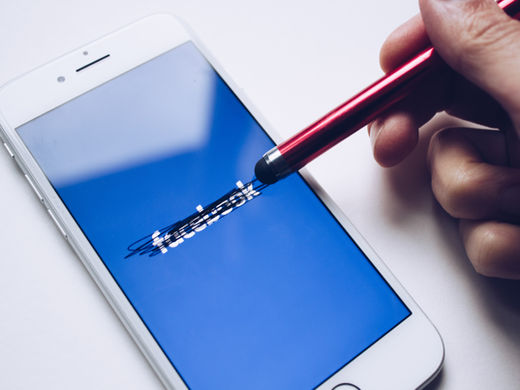 A hand uses a red stylus to scribble over the Facebook logo on a smartphone screen, symbolizing digital disconnection.