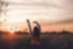 A woman walking in a field at sunrise with her arms in the air feeling free and happy