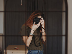 Woman photographing her reflection in a dark-framed mirror, representing self-reflection and a personal September reset.