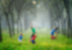 Children joyfully jumping on lush green grass, surrounded by dense trees. Image depicting outdoor play, nature, and childhood fun. Vibrant forest backdrop with active kids.